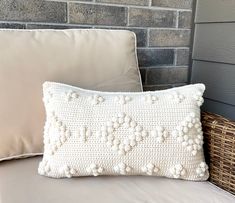 a white crocheted pillow sitting on top of a bed next to a wicker basket