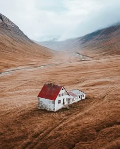 an abandoned house sits in the middle of a barren field with mountains in the background