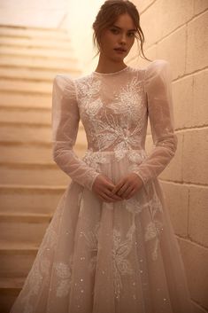 a woman in a white dress standing next to a brick wall with her hands on her hips