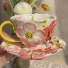 a hand holding a cup and saucer with flowers on it