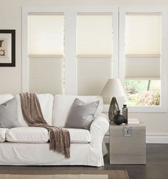 a living room with white couches and two windows covered in shades of light gray