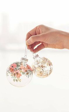 a hand is holding two ornaments with flowers painted on them and hanging from the strings