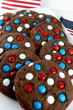 chocolate cookies decorated with red, white and blue candies are on a plate next to an american flag