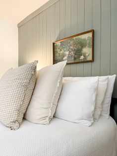 a bed with four pillows on top of it and a painting above the headboard