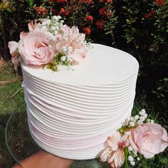 a large white cake with pink flowers on top and greenery in the back ground