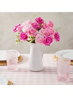 pink roses are in a white pitcher on a table with plates and utensils