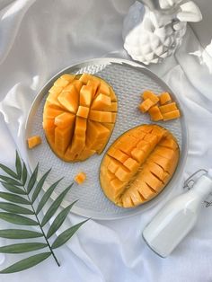 two pieces of mango on a plate next to a bottle of milk and a palm leaf