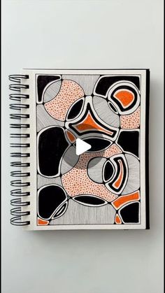 an open spiral notebook on top of a white surface with black and orange designs in the middle