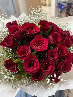 a bouquet of red roses sitting on top of a white table cloth with baby's breath