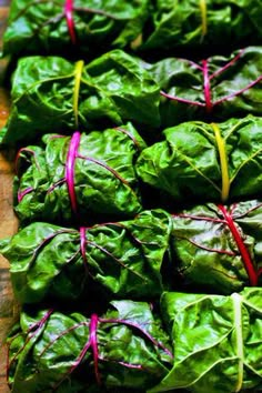 some lettuce wrapped in red string on top of a wooden cutting board next to other green leafy vegetables