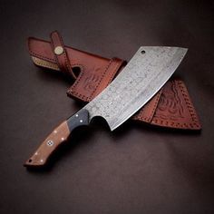 two knives sitting next to each other on top of a brown leather case with an intricate design