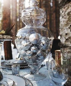 a glass vase sitting on top of a table covered in silver plates and glasses next to a tree