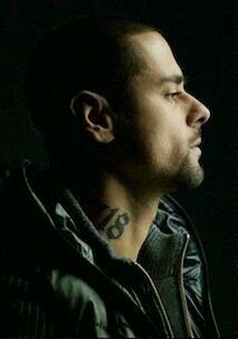 a man with a tattoo on his neck looking off to the side in front of a dark background