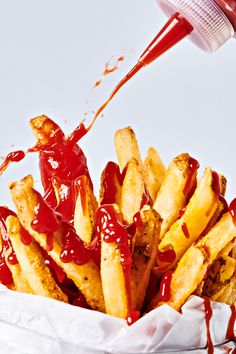 french fries with ketchup being drizzled over them in a basket