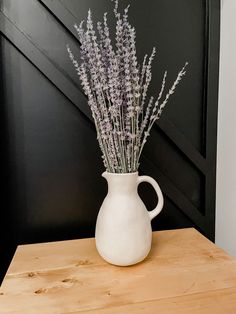 a white vase filled with lavender flowers on top of a wooden table next to a black door