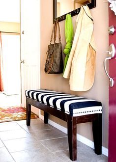 a bench sitting in front of a door with bags hanging on the hooks and purses