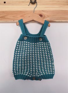 a blue and white knitted overall hanging on a wooden hanger