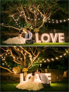 a couple sitting on the ground in front of a love sign with lights hanging from it