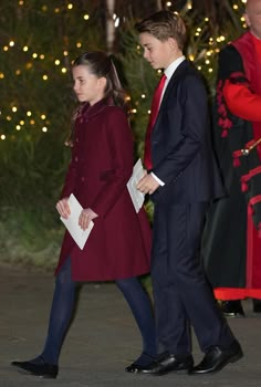 a man and woman walking next to each other in front of a christmas tree at night