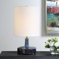 a blue table lamp sitting on top of a wooden desk next to a vase with flowers