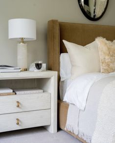 a bedroom with a white bed, nightstand and mirror on the wall above it's headboard