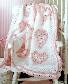 a white crocheted blanket with pink hearts on it sitting next to a rocking chair