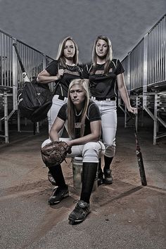 three women in baseball uniforms posing for a photo with bats and ball gloves on their feet