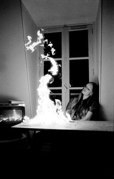 a woman sitting in front of a window with fire coming out of her mouth and hands