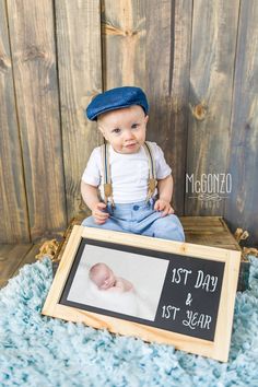 a baby in overalls and a hat sitting next to a sign