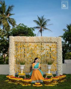 a woman sitting on top of a lush green field next to a flower covered wall