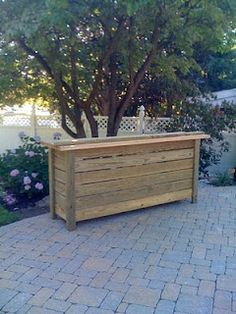 a large wooden planter sitting on top of a brick patio next to a tree