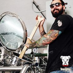 a bearded man holding a baseball bat in front of a mirror and drum set with other instruments behind him