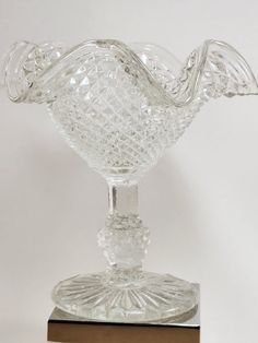 a clear glass vase sitting on top of a wooden base with an intricate design in the center