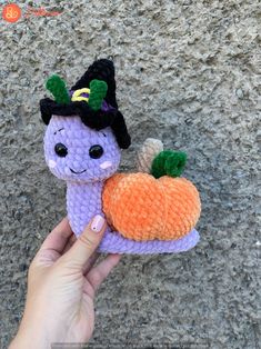 a hand holding a small purple stuffed animal with a pumpkin on it's back