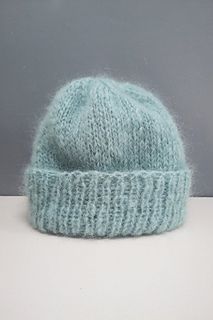 a light blue knitted hat sitting on top of a white table next to a gray wall