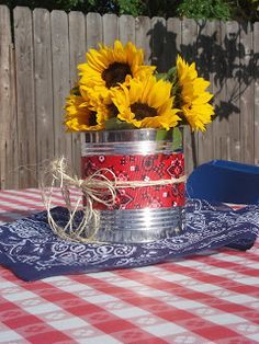 sunflowers in a tin can sitting on a table with a red and white checkered tablecloth