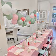 a long table with pink, green and white balloons hanging from it's ceiling