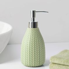 a green soap dispenser sitting on top of a counter next to a white bowl