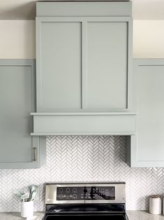 a stove top oven sitting inside of a kitchen next to gray cabinets and white counter tops