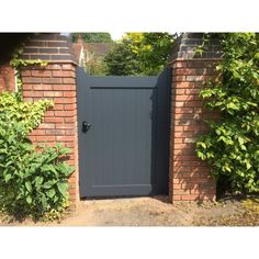 an open gate in the middle of a brick wall with green plants growing around it