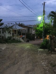 an empty dirt road in the middle of a small village at night with power lines overhead