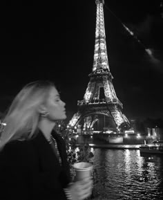 a woman standing in front of the eiffel tower at night with her drink