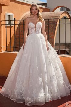 a woman in a white wedding dress standing on a balcony with an orange building behind her