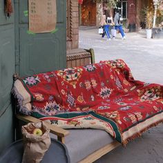 a couch that is covered with a blanket on the ground in front of a building