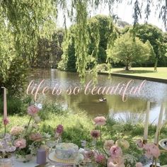 there is a table with flowers and cake on it in front of a lake that says, life is so beautiful