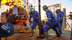 three men in blue work on an oil rig