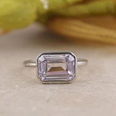 a ring with an amethorate stone in the center on a table next to a yellow flower