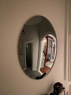 a round mirror hanging on the side of a wall next to a book shelf filled with books