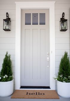 a white front door with two planters on either side and the word hello written on it