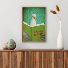 a white bird sitting on top of a green book cover next to a vase filled with flowers